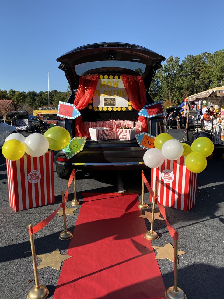 an open trunk with popcorn boxes and balloons on the ground next to red carpeted area