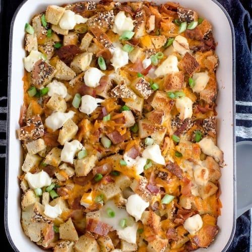 a casserole dish with potatoes, bacon and green onions in it on a black surface