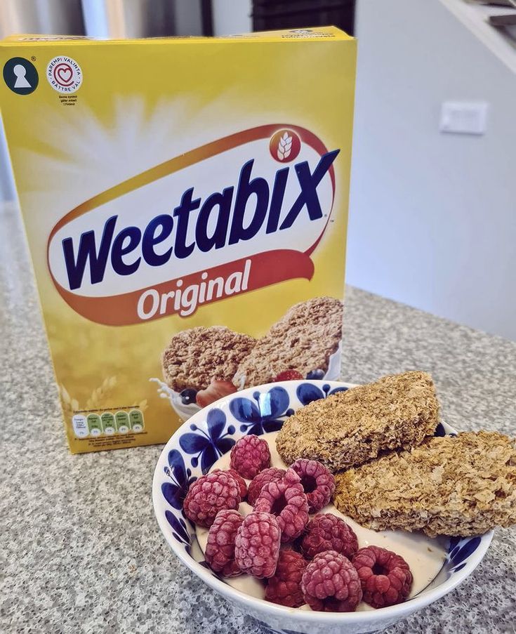 a box of weetabix next to a bowl of cereal and raspberries