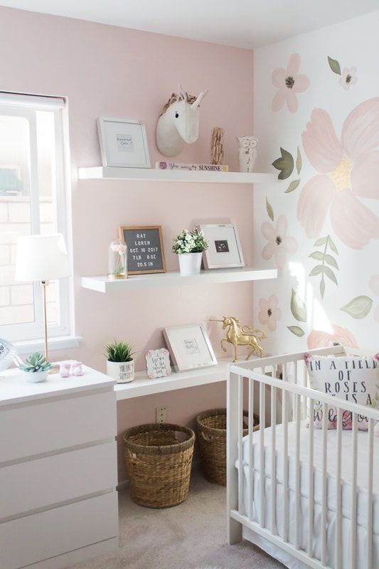 a baby's room with pink and white flowers painted on the walls, shelves above a crib