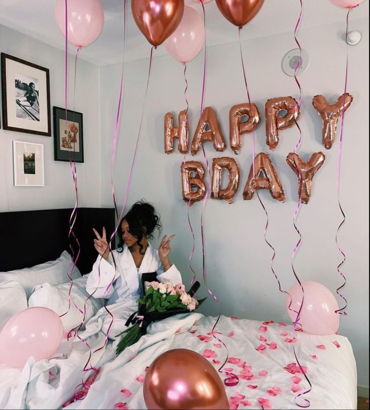 a woman is sitting on her bed with balloons and streamers in front of her