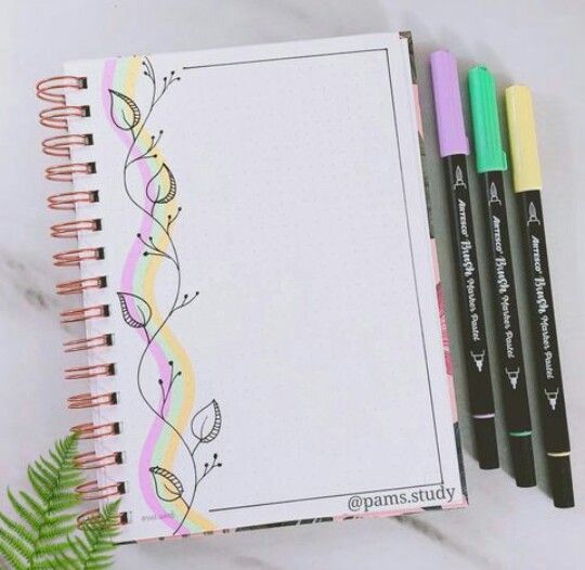 an open notebook with three markers next to it and a fern plant on the side