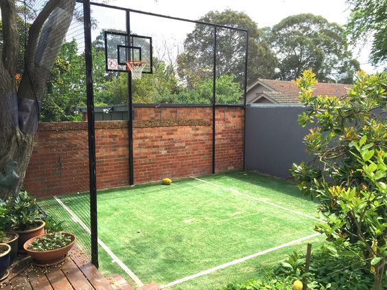 a backyard with a basketball court, potted plants and a tree in the background