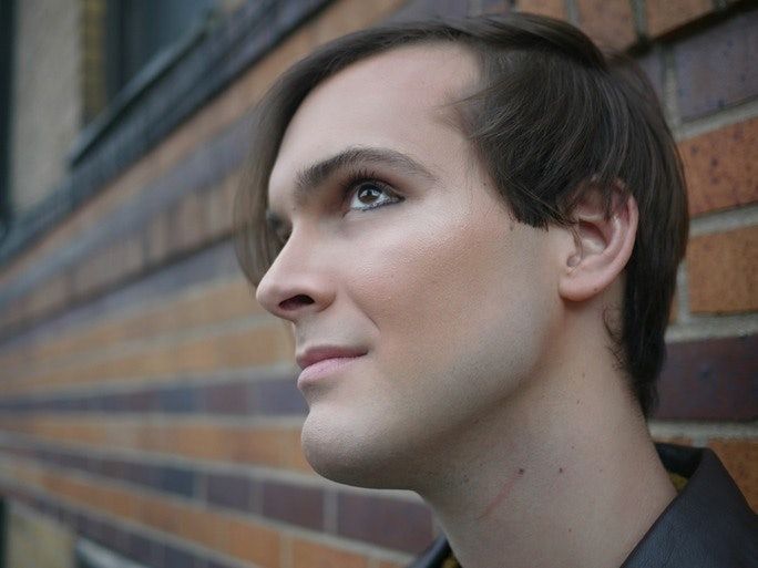 a man standing in front of a brick wall with his eyes closed and looking off to the side