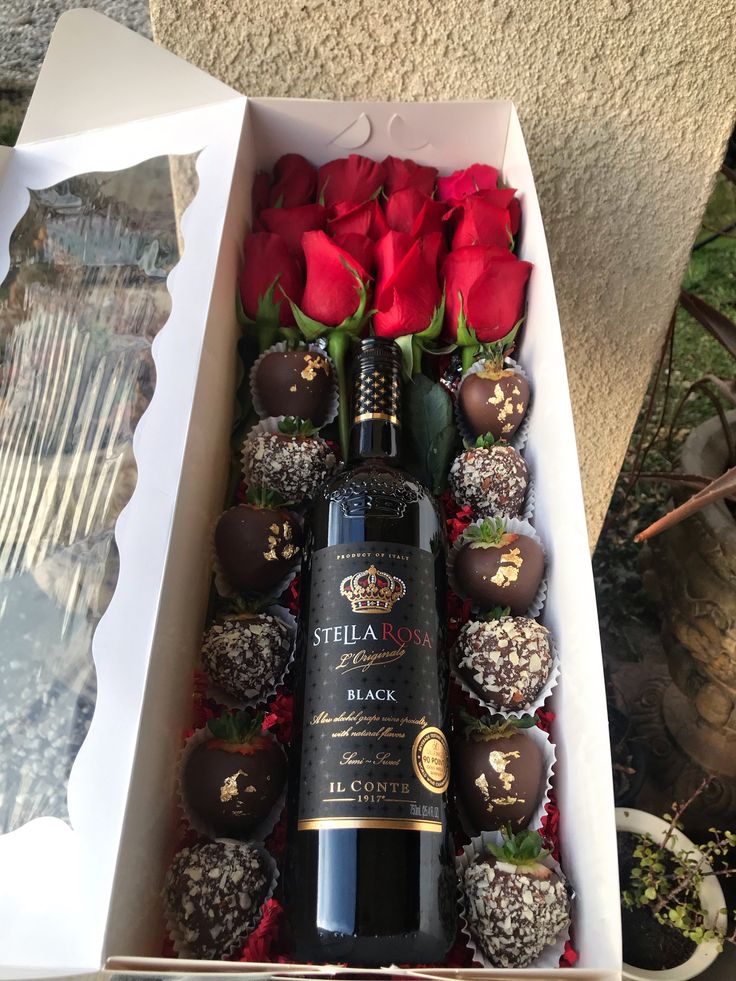 a wine bottle in a box with chocolates and roses on the table next to it