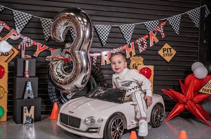 a young boy sitting on top of a toy car in front of a birthday decoration