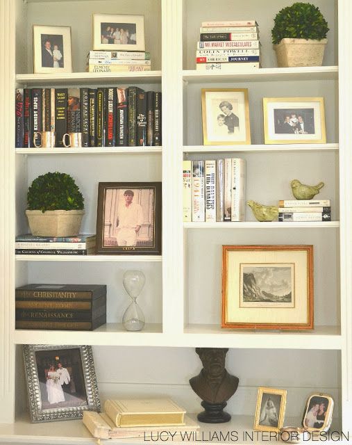 a white book shelf filled with lots of books and framed pictures on top of it