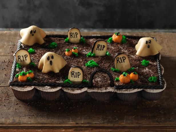 a halloween cake with ghost cookies and tombstones on the top, sitting on a wooden table