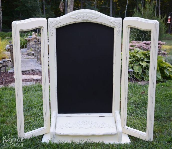 an old white painted wooden frame with chalkboard in the middle and grass around it