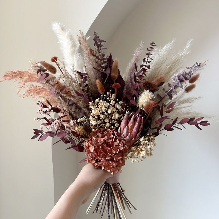 a hand holding a bouquet of dried flowers