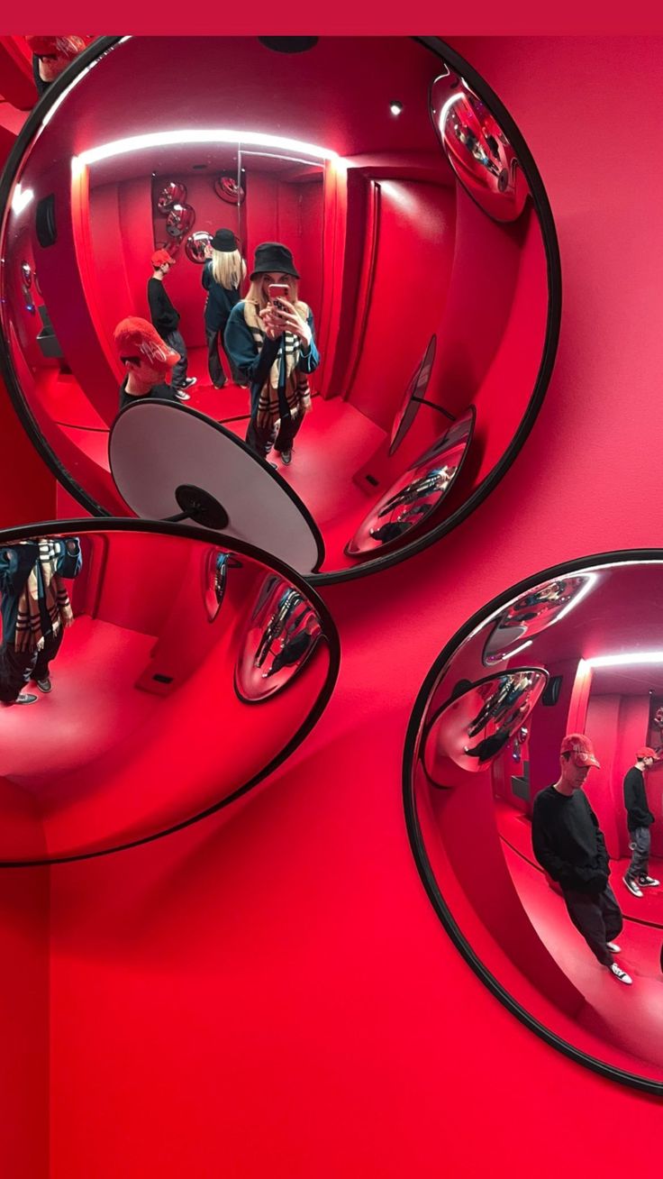 three mirrors reflecting people in the reflection of them on a red wall with pink walls