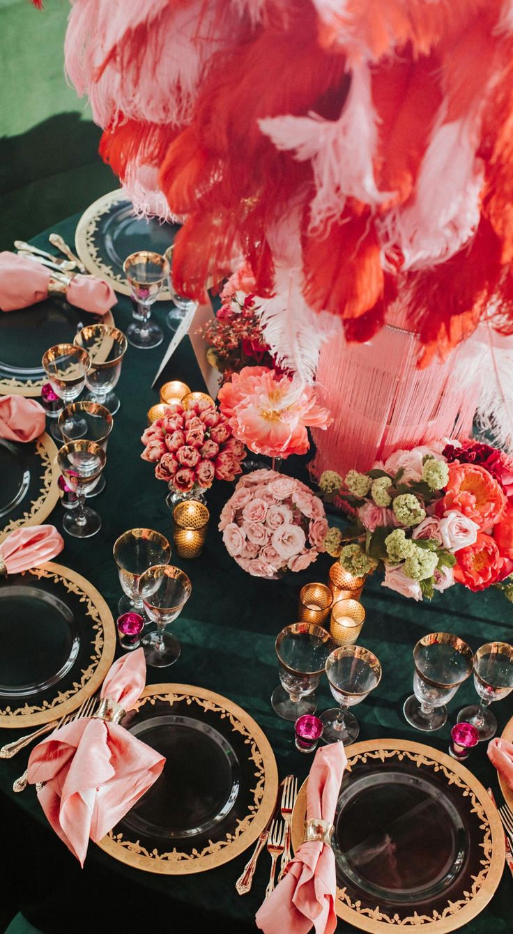 the table is set with pink and gold plates, place settings, and feathers on it