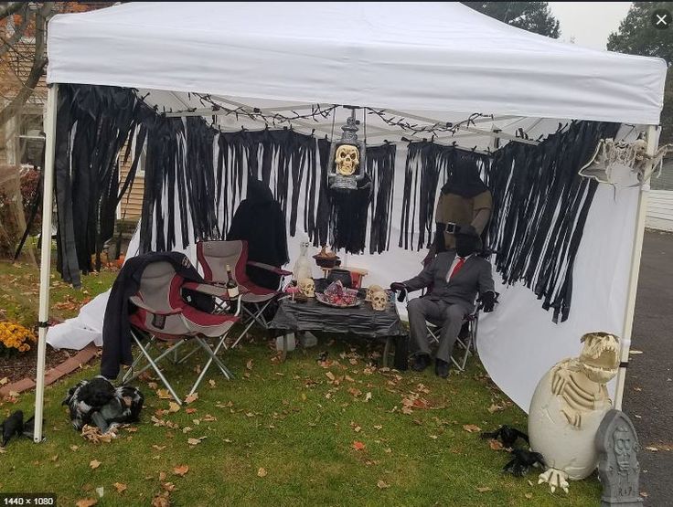 two people sitting in lawn chairs under a white tent with black tassels on it