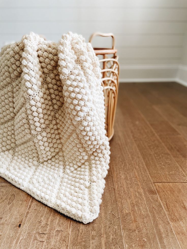 a white knitted blanket sitting on top of a wooden floor next to a basket