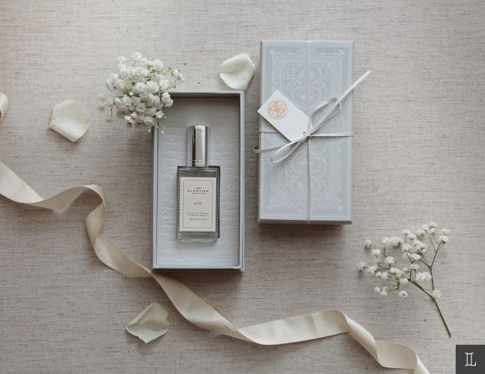 a bottle of cologne sitting next to a box with ribbon and flowers in it on top of a table