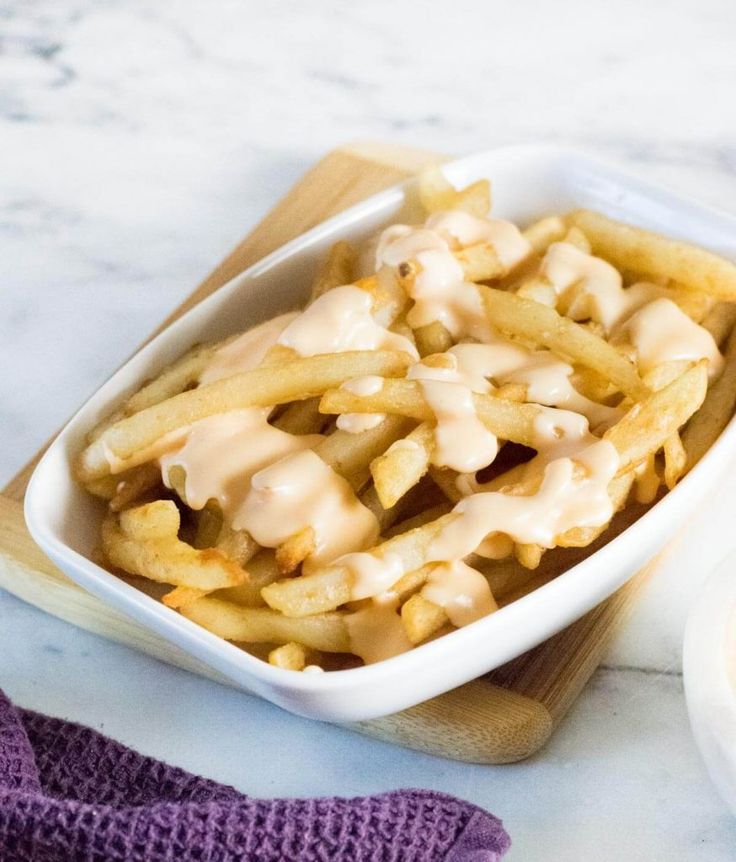 french fries in a white dish on top of a wooden cutting board next to a bowl of sauce