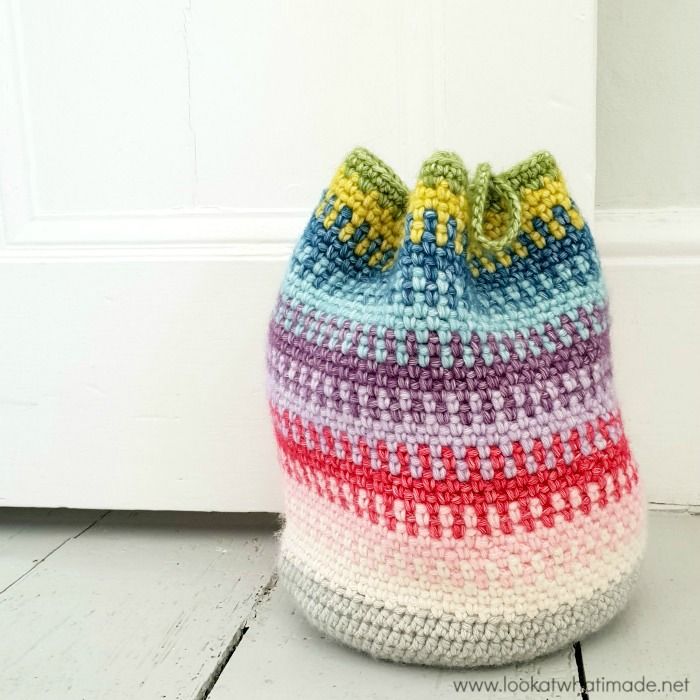 a crocheted bag sitting on the floor next to a white door with a green bow