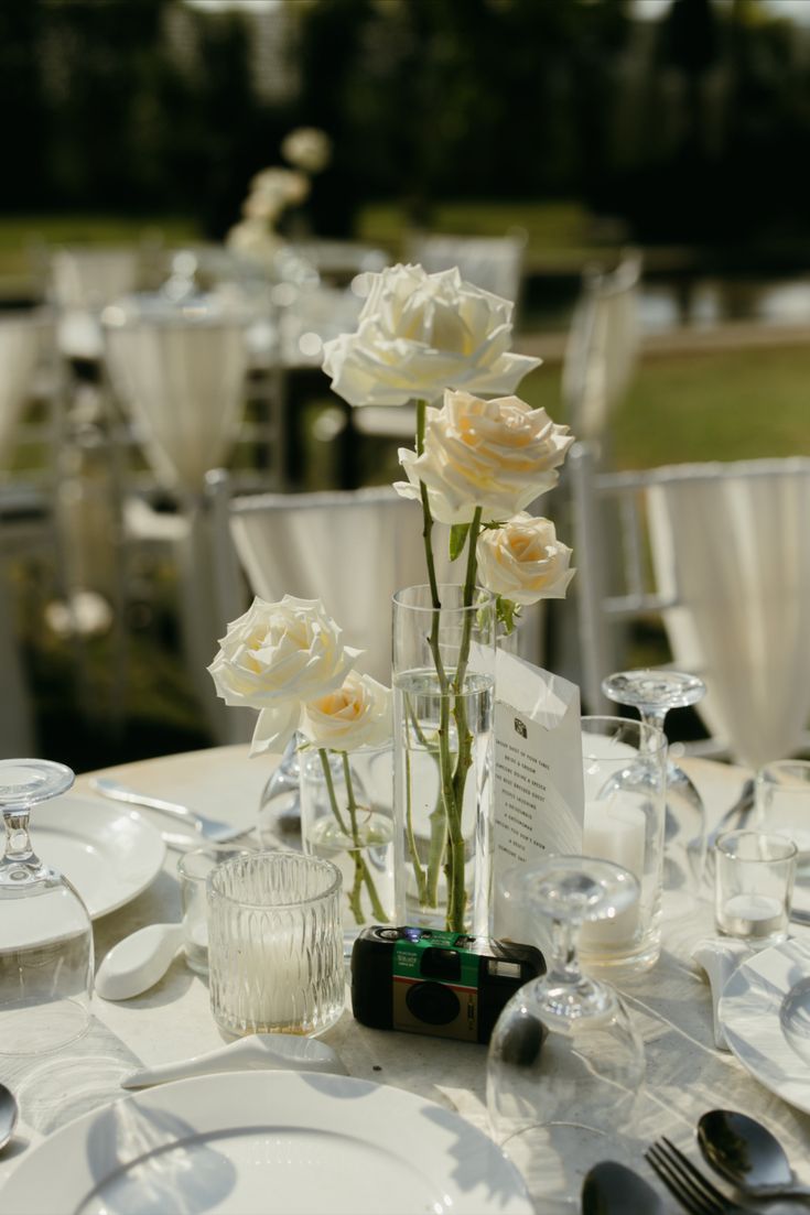 the table is set with white plates and silverware, flowers in glass vases