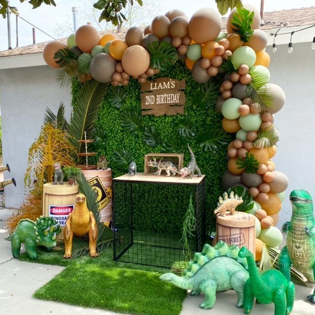 an outdoor birthday party with balloons and dinosaur figurines in front of the entrance