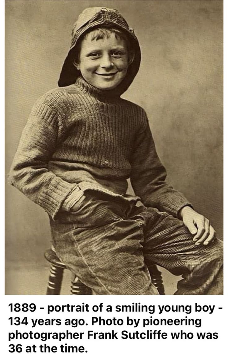 an old photo of a young boy wearing a hat and sweater, sitting on a chair