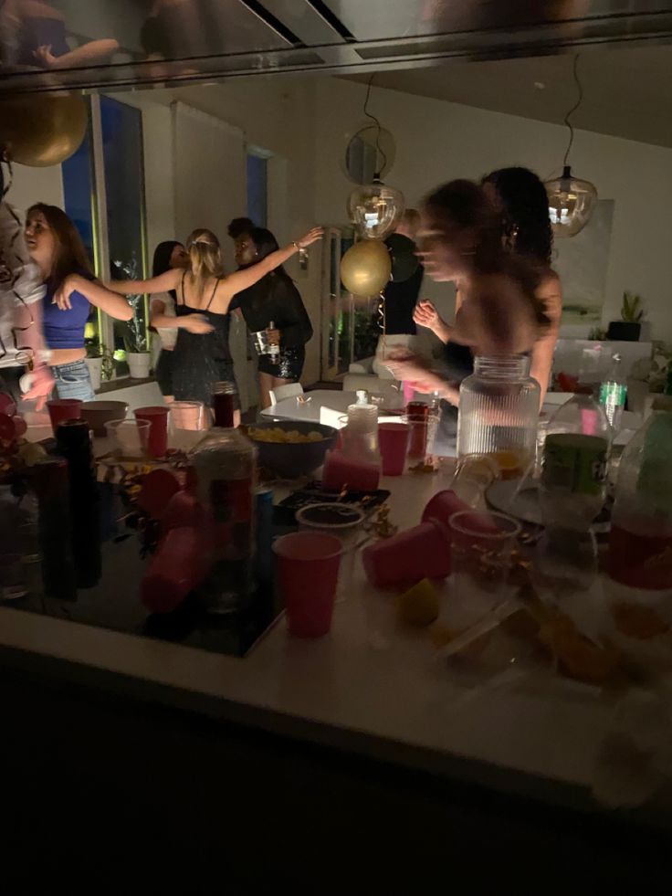 a group of people standing in front of a counter filled with bottles and glasses on it