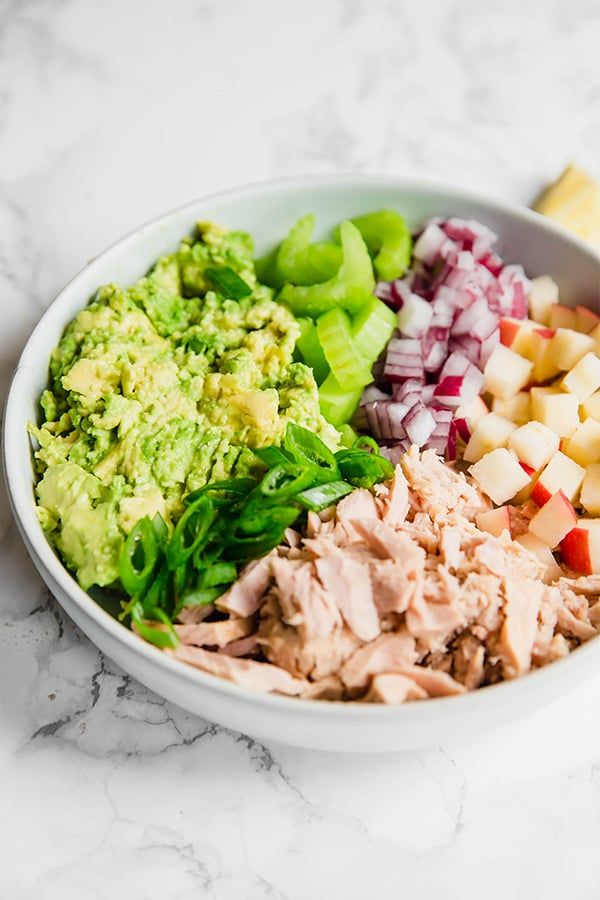 a white bowl filled with meat, vegetables and fruit on top of a marble counter