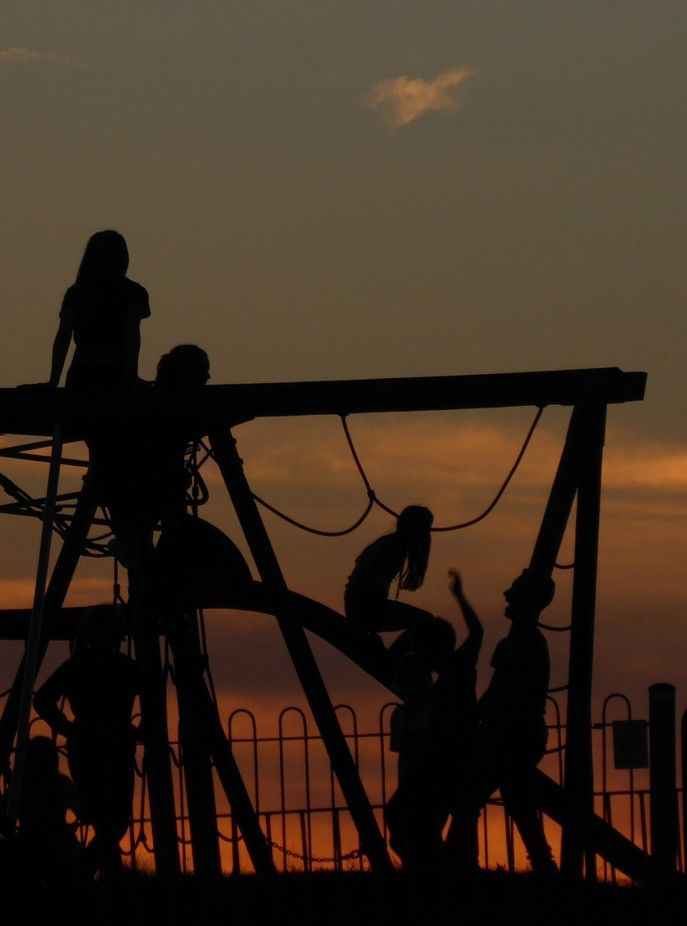 silhouettes of children playing on a playground at sunset