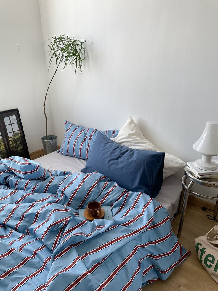 a bed with blue and red striped sheets in a room next to a potted plant