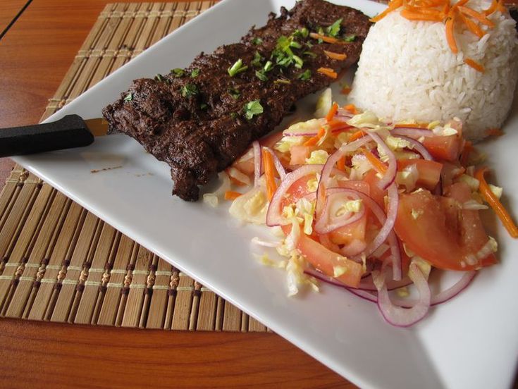 a white plate topped with meat and vegetables next to rice on top of a wooden table