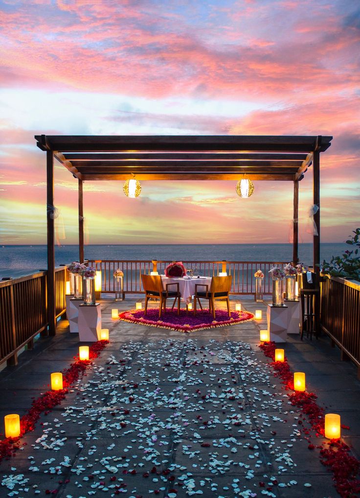 an outdoor dining area with candles and flowers on the ground, overlooking the ocean at sunset