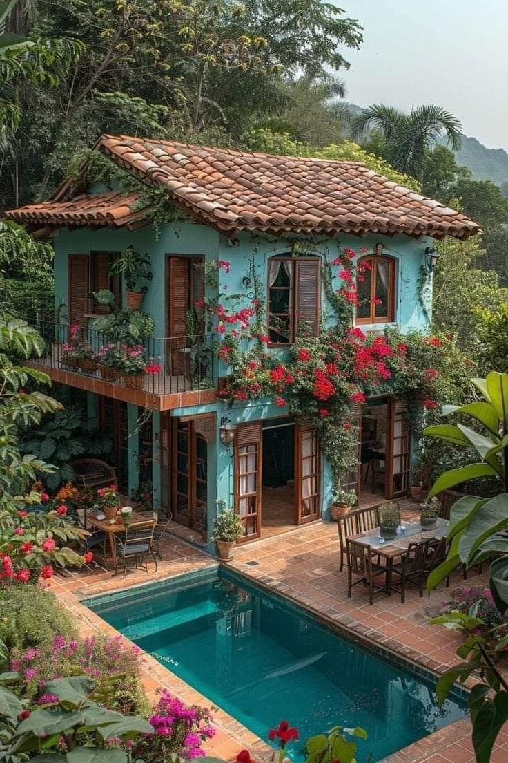 an outdoor swimming pool surrounded by greenery and flowers with a house in the background