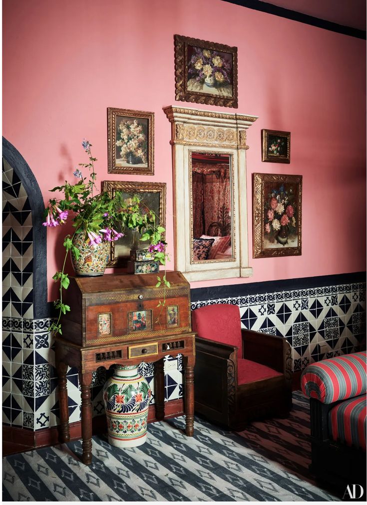 a living room with pink walls and paintings on the wall, an old desk in front of a mirror