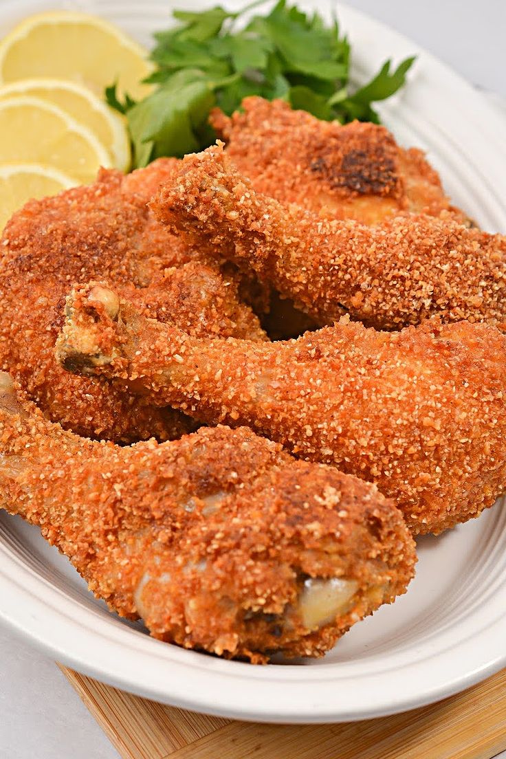 some fried food on a white plate with lemon wedges and parsley next to it