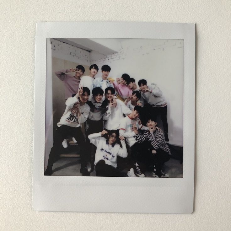 a group of young men posing for a photo in front of a white wall with a polaroid frame