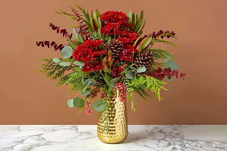 a gold vase filled with red flowers and greenery