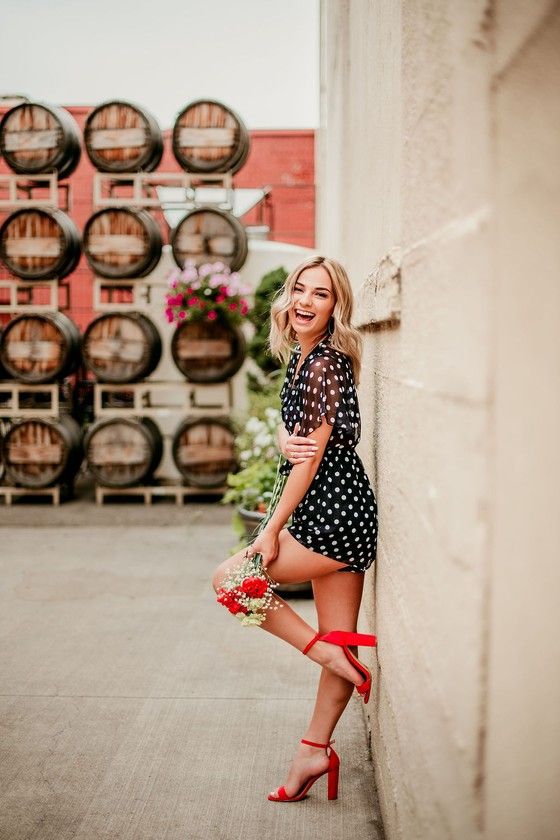 a woman leaning against a wall with wine barrels behind her and holding a basket full of flowers