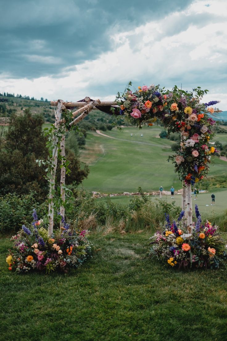 an outdoor wedding setup with flowers on the arch and greenery in the foreground