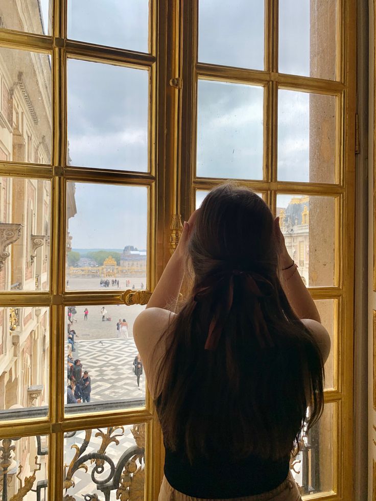 a woman standing in front of a window looking out