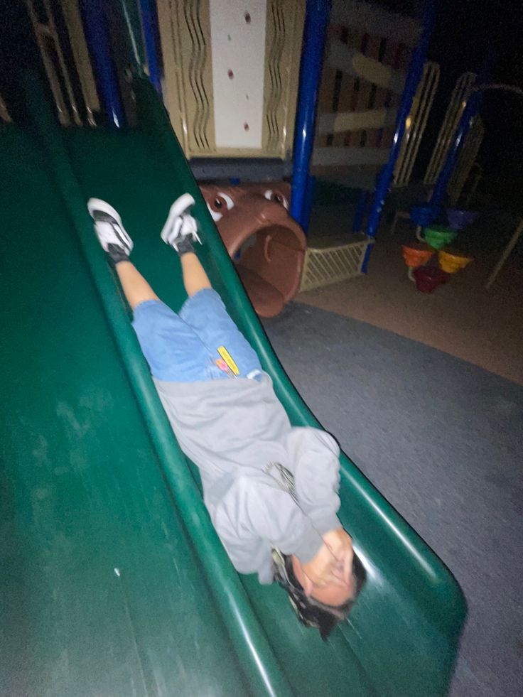 a young boy laying on top of a green slide