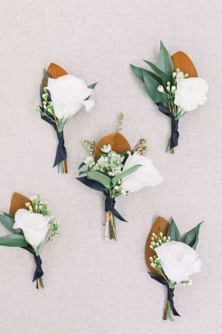 six boutonnieres with white flowers and greenery are arranged on the wall