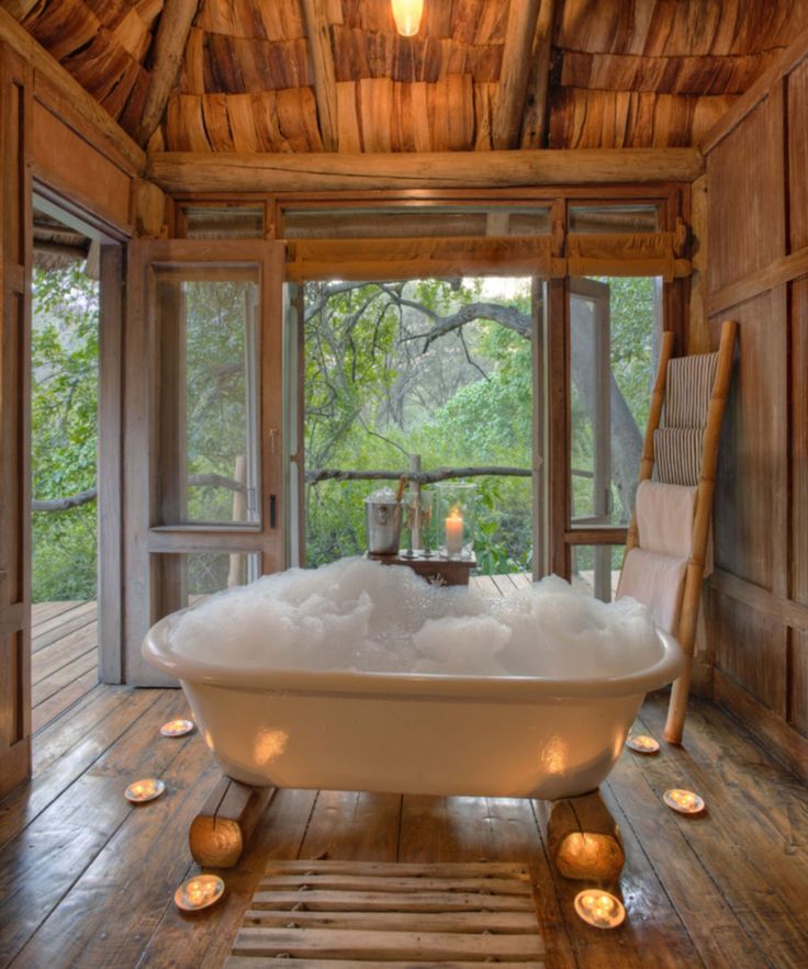 a bathtub in the middle of a wooden floored room with candles around it