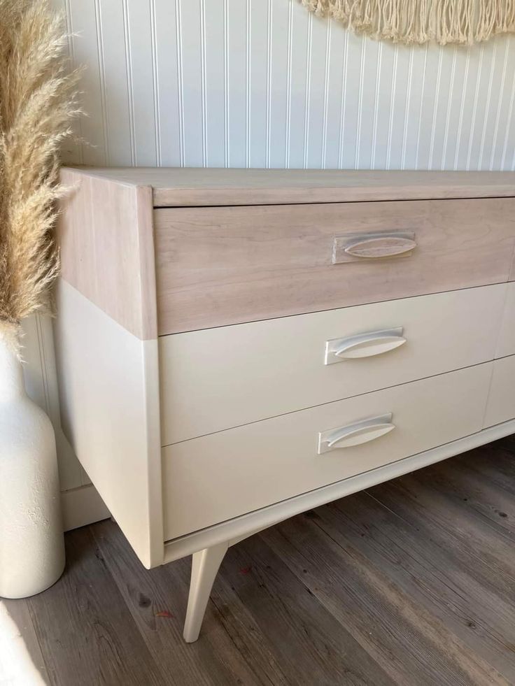 a white vase sitting on top of a wooden floor next to a dresser with drawers