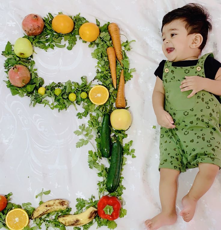 a baby laying next to a letter made out of fruits and vegetables