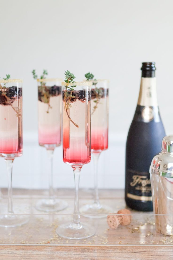 three glasses filled with different colored drinks next to a bottle and corkscrews