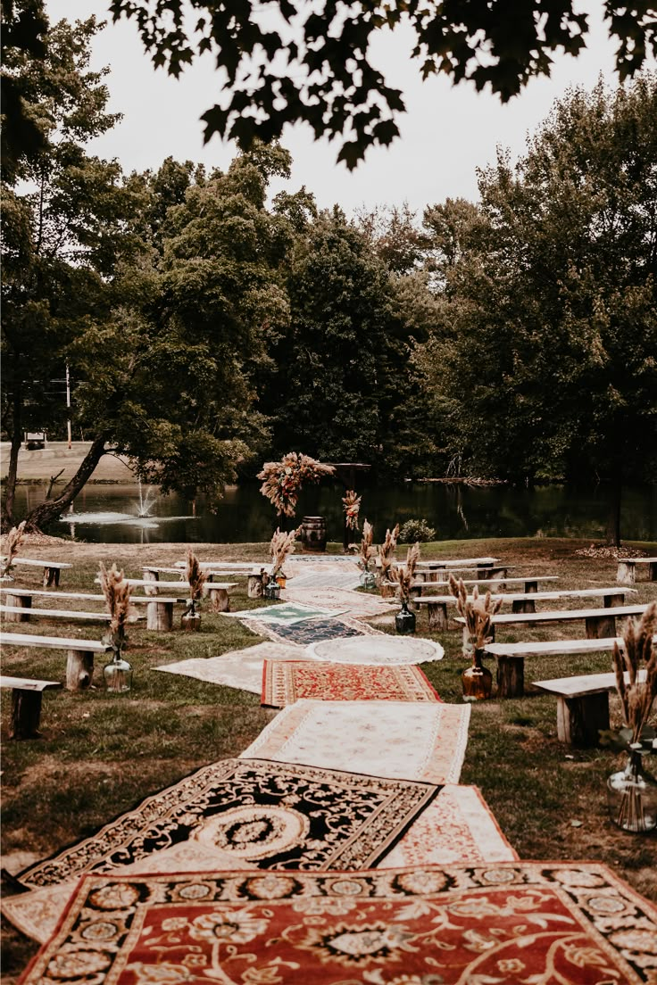 an outdoor wedding ceremony with rugs and flowers on the aisle, surrounded by trees