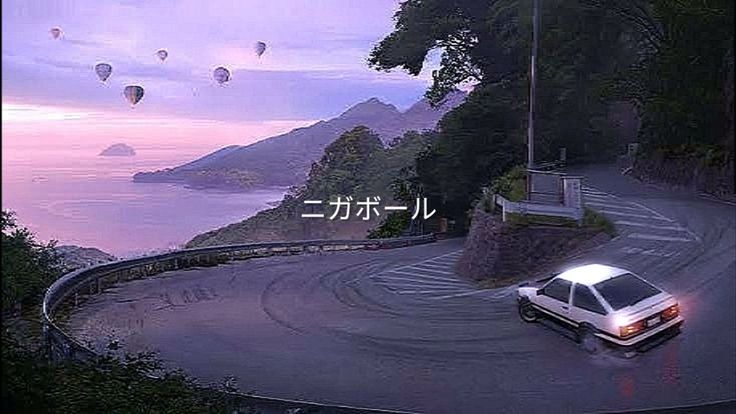 a white car driving down a winding road next to the ocean with hot air balloons in the sky