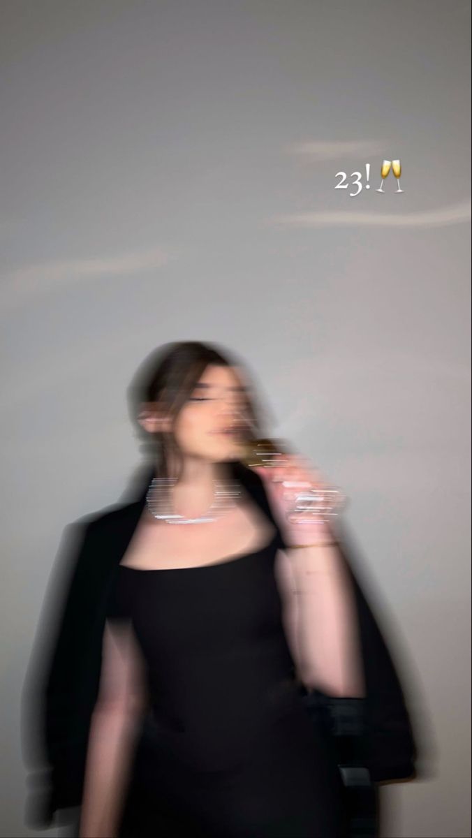 a blurry photo of a woman in a black dress drinking from a wine glass