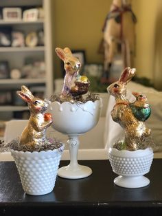 three bunny figurines sitting on top of a white egg in a vase with two smaller ones