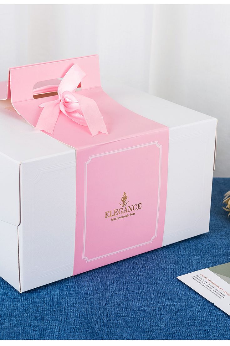 a pink and white box with a bow on the top sitting on a blue surface