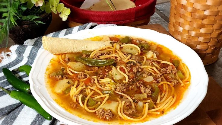 a white plate topped with pasta and meat next to a bowl of soup on top of a table